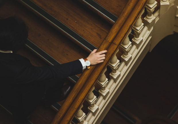 A photo of a suited man's hand holding a traditional bannister